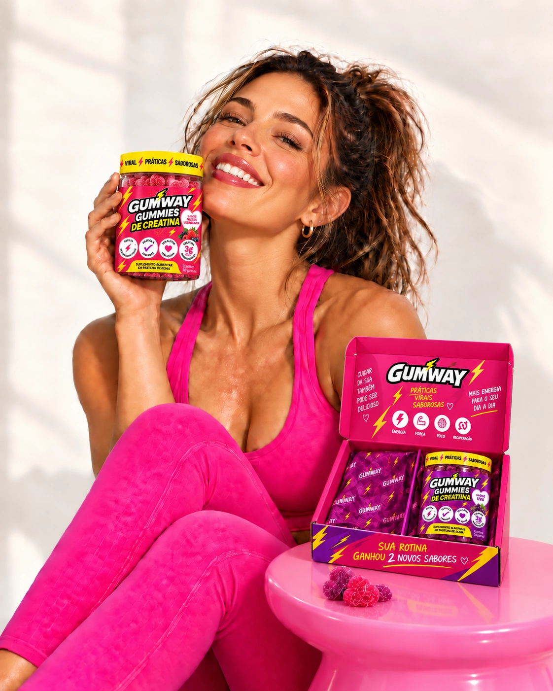 Mulher com roupa de treino pink segurando Gumway Frutas Vermelhas, com a caixa aberta e o pote Uva sobre a mesa